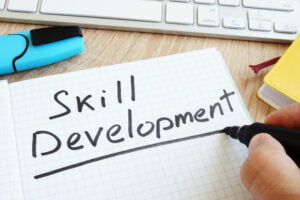 Hand holding black pen writing 'skill development' in notebook