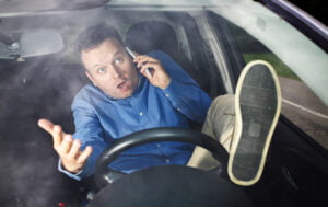 Unsafe driver using mobile phone with foot on steering wheel 