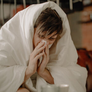 Man covered with a duvet sneezing into a tissue