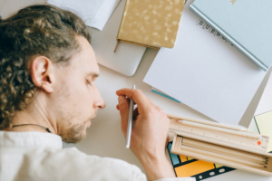 Exhausted employee asleep over paperwork with pen in hand