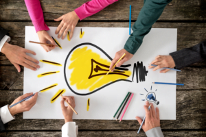 Multiple people's hands working on a drawing of a light bulb