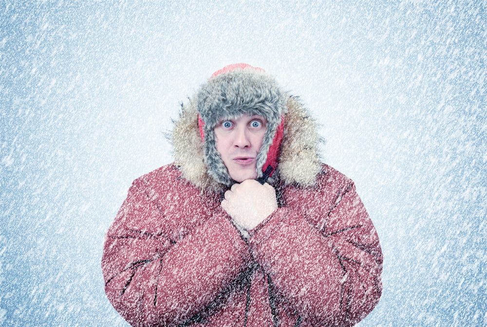 Middle-aged man dressed in a big jacket and hat while it's snowing, visibly cold