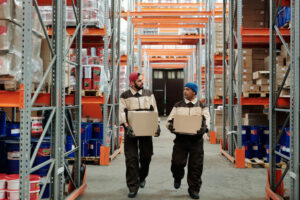 Two warehouse employees walking side by side, carrying boxes