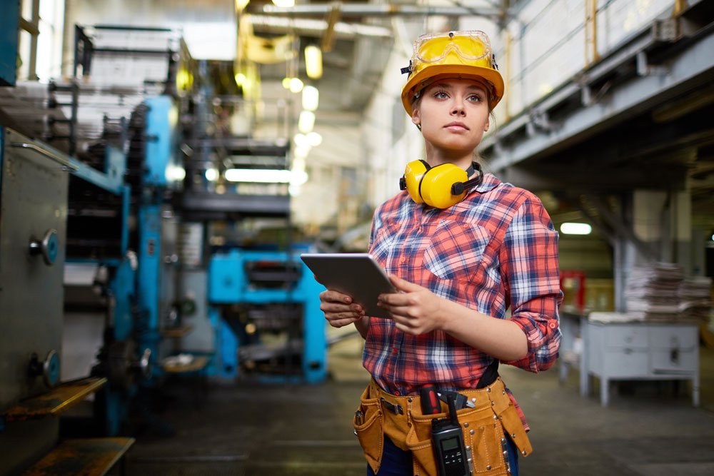 Woman on construction site wearing a protective hat and holding a clipboard.