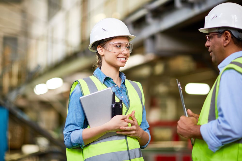 Woman wearing a safety hat and a hi-vis speaking to male colleague