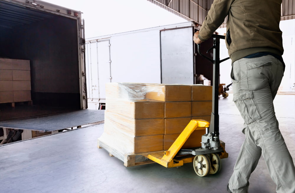 Worker using pallet truck to move large packages
