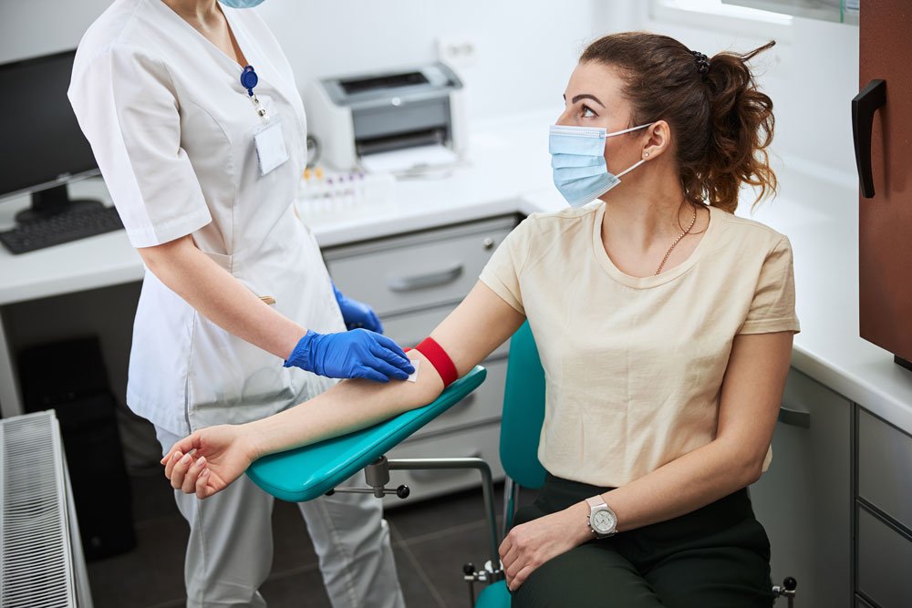 Woman in medical mask being prepared for venipuncture.