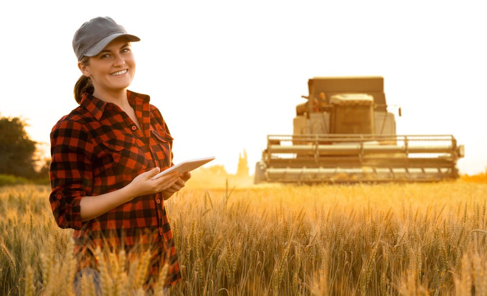 Farmer holding a tablet standing in the field with harvester in background