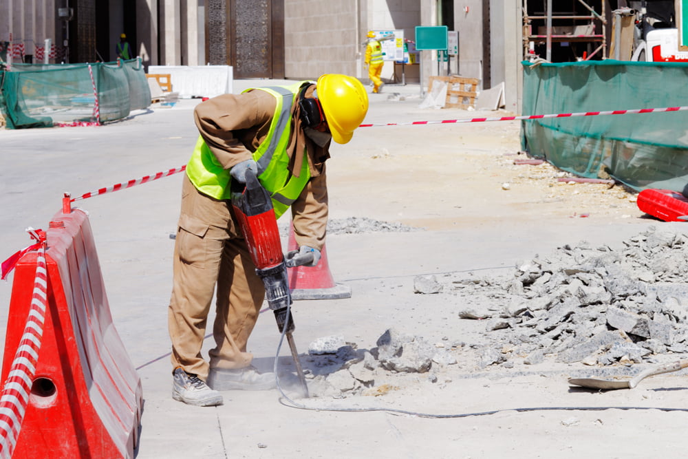Worker using jackhammer to break through asphalt