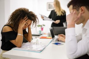 A man and woman with their hands to their forehead illustrating work-related health issues.