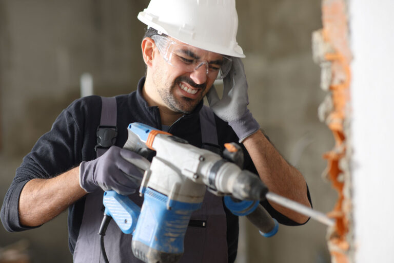 a man with driller in hand and one hand over his ear.