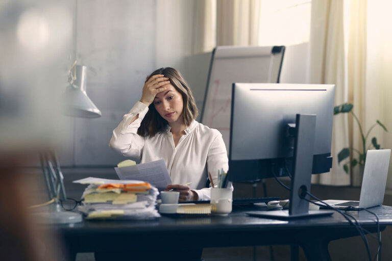 A woman at work desk with her hand on her head.